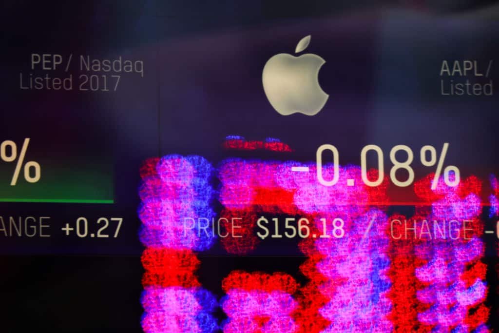 Het logo van Apple met op de achtergrond paarse en rode cijfers van de beurs.