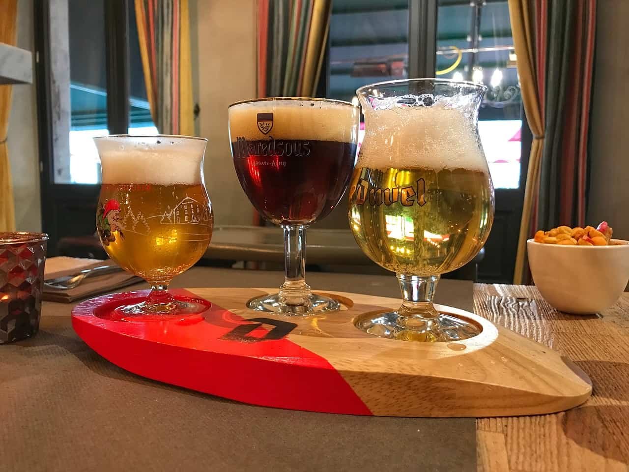 Chouffe, Maredsous et Duvel, trois verres de bière belge côte à côte sur une planche de bois.