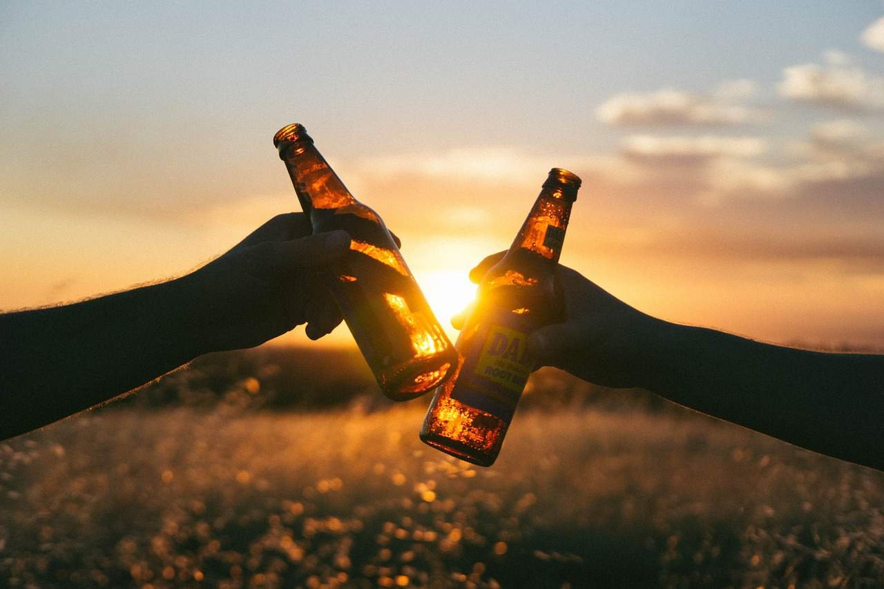 Deux bouteilles de bière sonnent l'une contre l'autre avec le soleil couchant à l'arrière-plan.