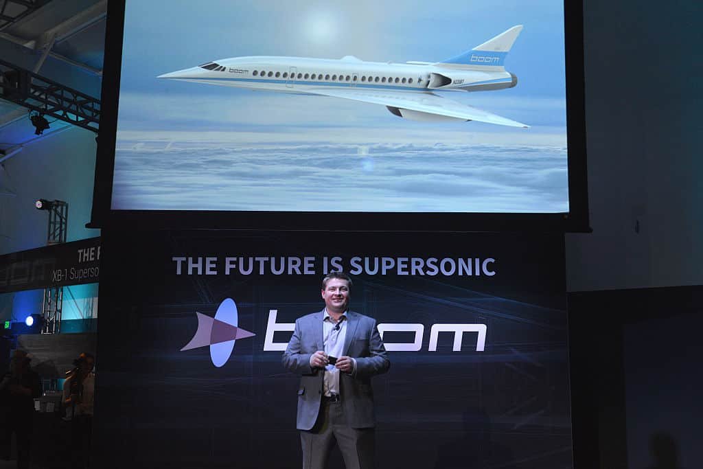 Blake Scholl staat te spreken voor een scherm waarop zijn nieuwe supersonisch vliegtuig afgebeeld staat.