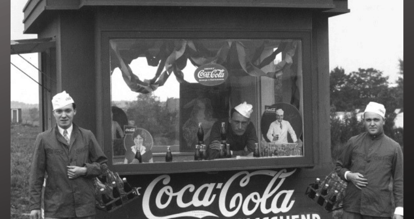 Mannen poseren in een kiosk die Coca-Cola verkoopt.