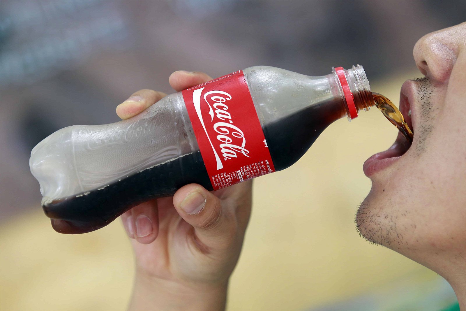 Een close-up van een flesje Coca-Cola dat door een man in z'n mond wordt gegoten.