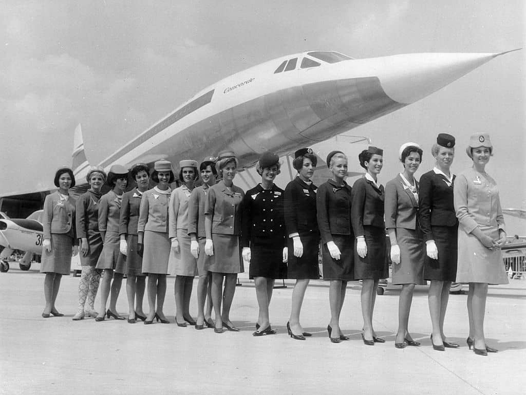Stewardessen staan netjes naast elkaar voor de Concorde op een beeld in zwart-wit.