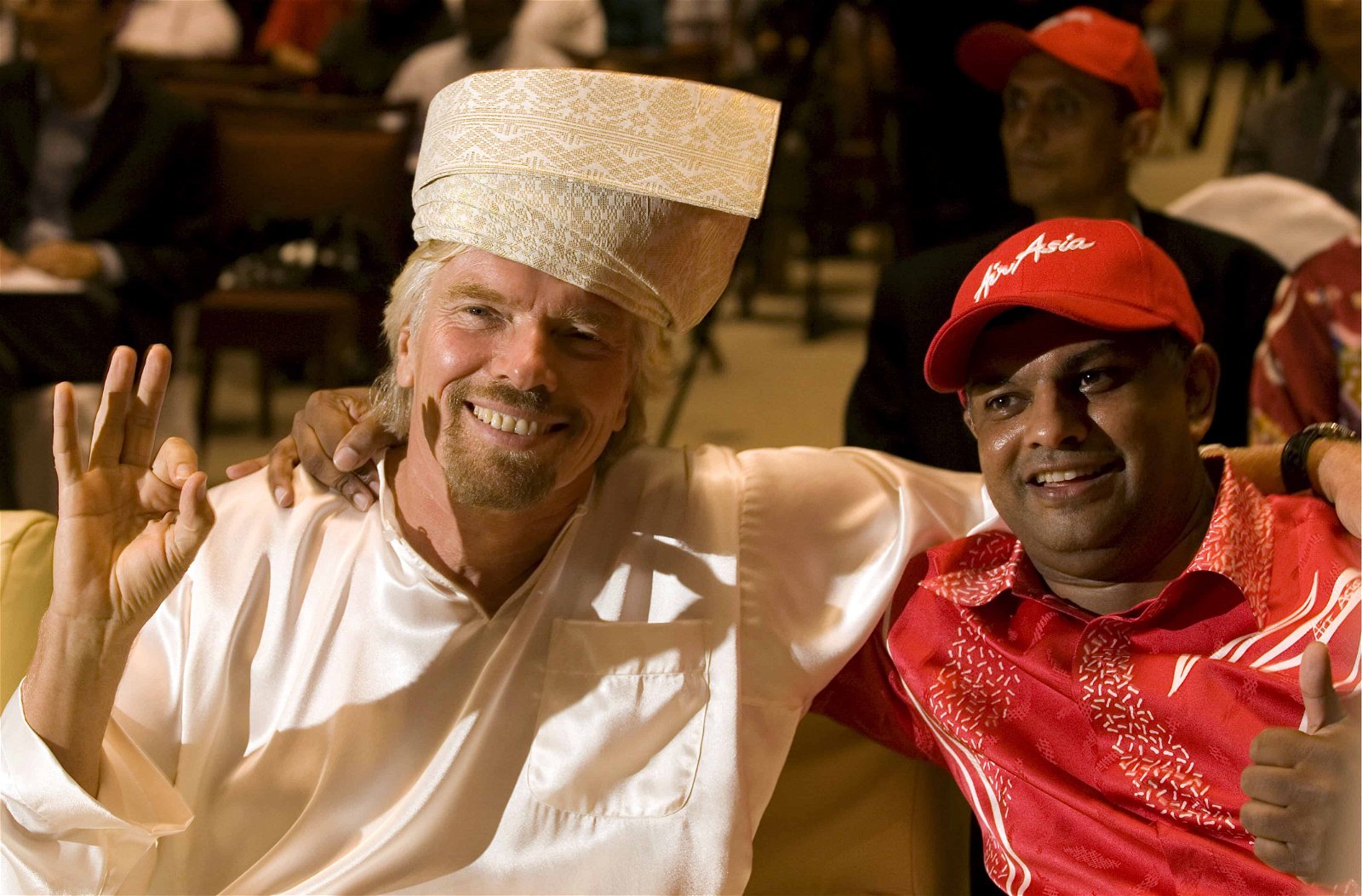 Richard Branson in lokale klederdracht naast een zwarte man in een rood pak.