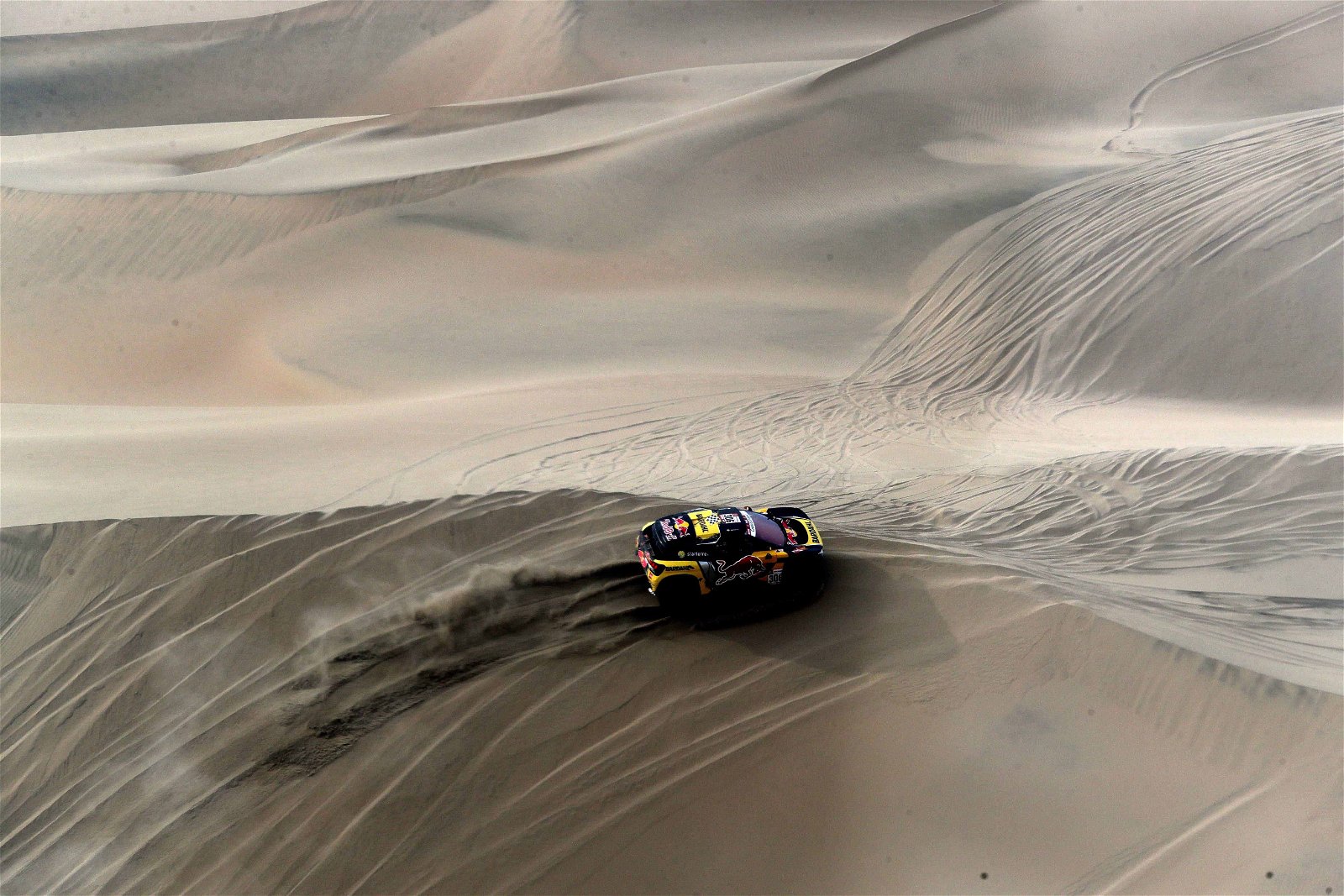 Een wagen rijdt met stofwolk over een duin in de woestijn tijdens de Dakar Rally.