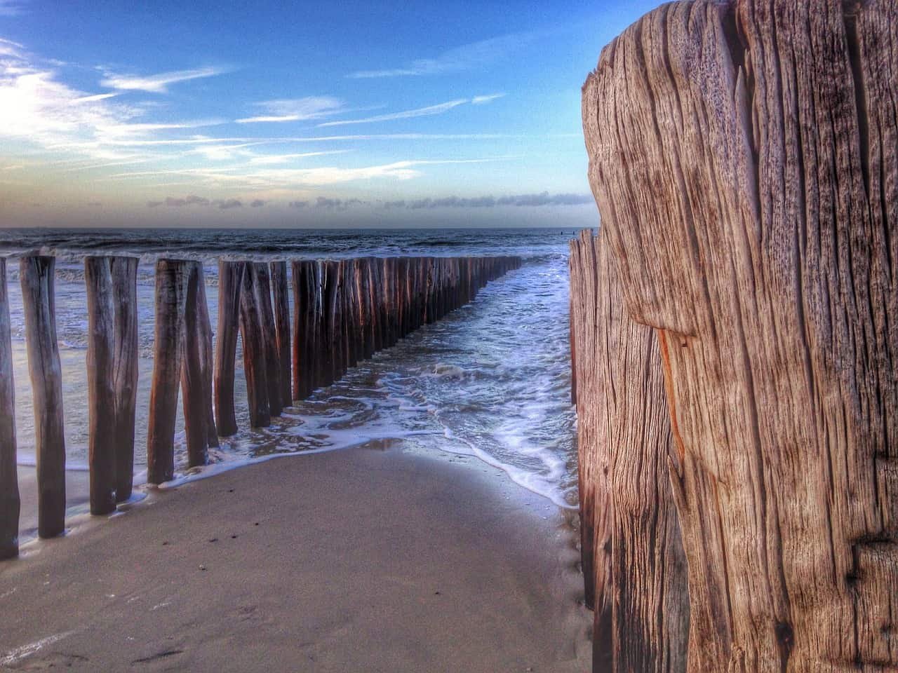 Zeewater spoelt aan op het strand tussen een reeks houten palen.
