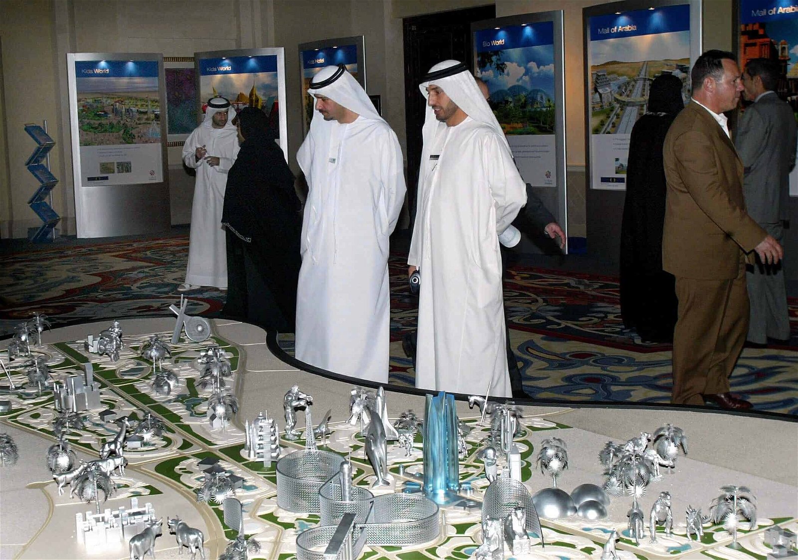 Twee mannen in een wit kleed kijken naar een grote maquette van Dubailand.