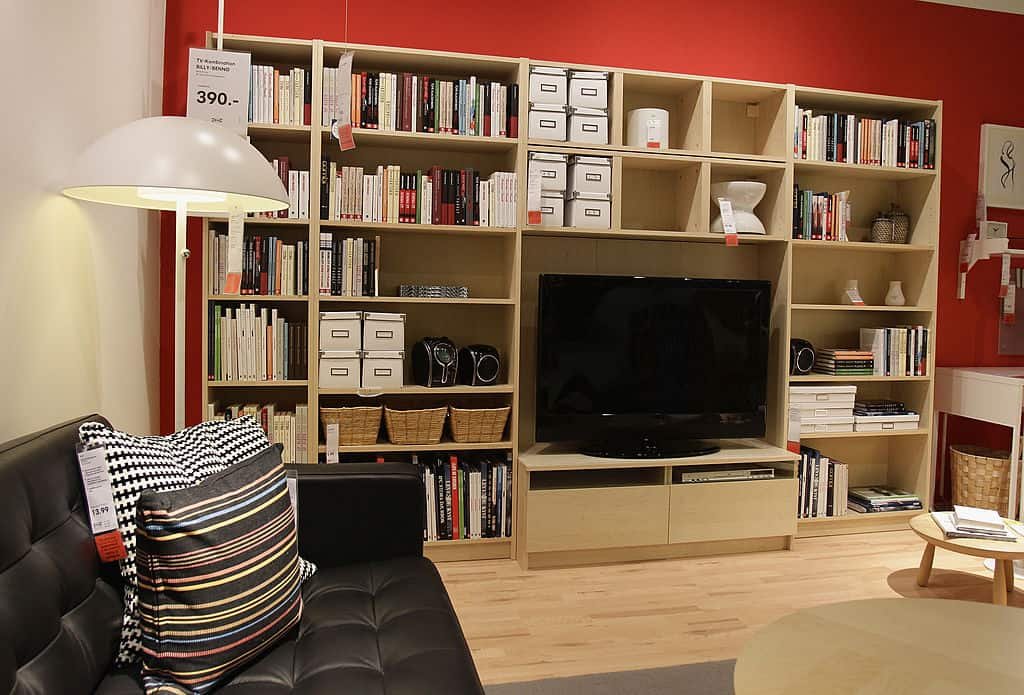 Een woonkamer in de etalage van een IKEA-winkel met een boekenkast vol boeken, een televisie en zetels.