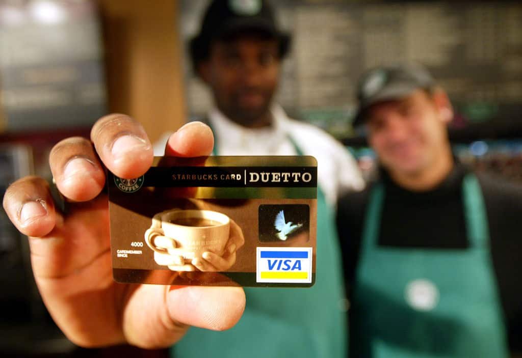 Een man houdt een kredietkaart met een foto van een kop koffie, de naam van Starbucks en het logo van VISA, vast.