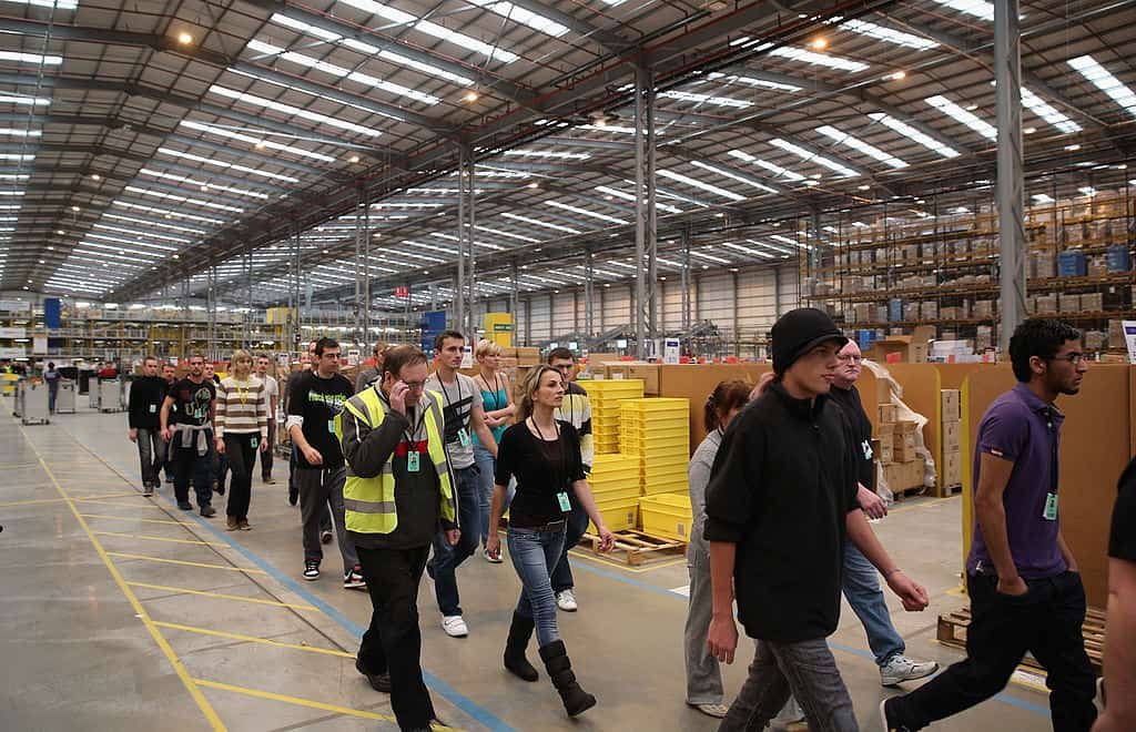 Medewerkers van Amazon lopen door een gangpad in een magazijn.