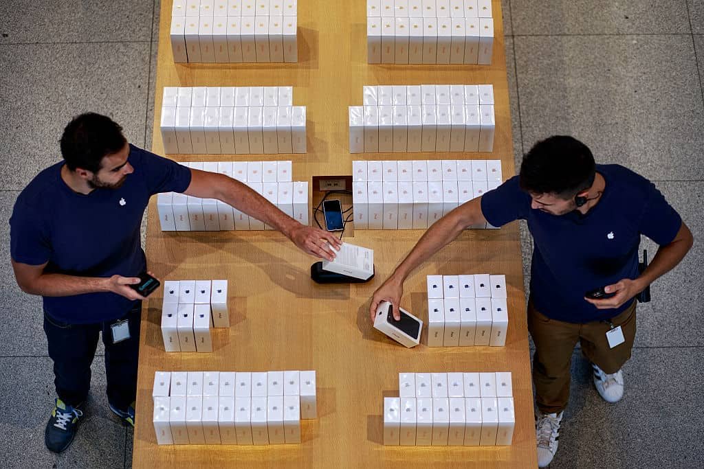 Twee medewerkers van Apple met in het midden een houten tafel vol doosjes met iPhones.