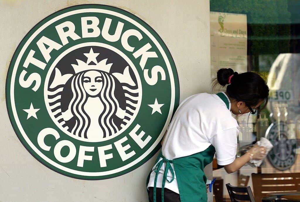 Een vrouw maakt een raam schoon rechts van het logo van Starbucks.