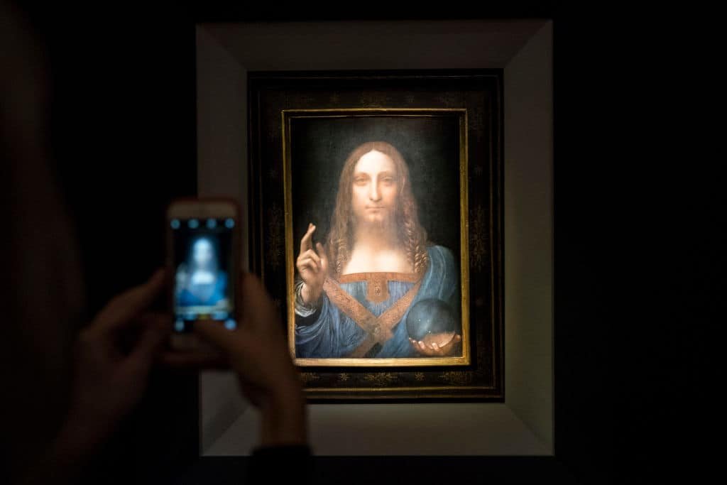 Een smartphone fotografeert een schilderij waarop Christus staat afgebeeld.