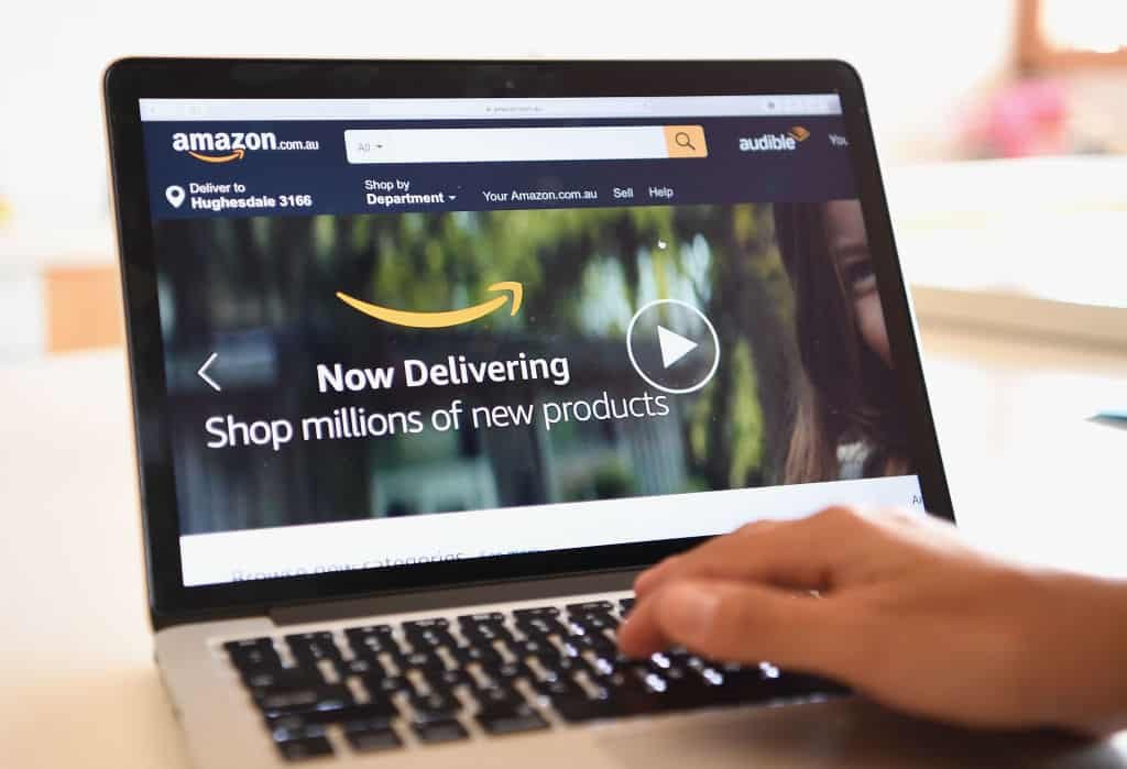 Een hand drukt op een toetsenbord van een laptop met op het scherm de homepagina van Amazon.com.
