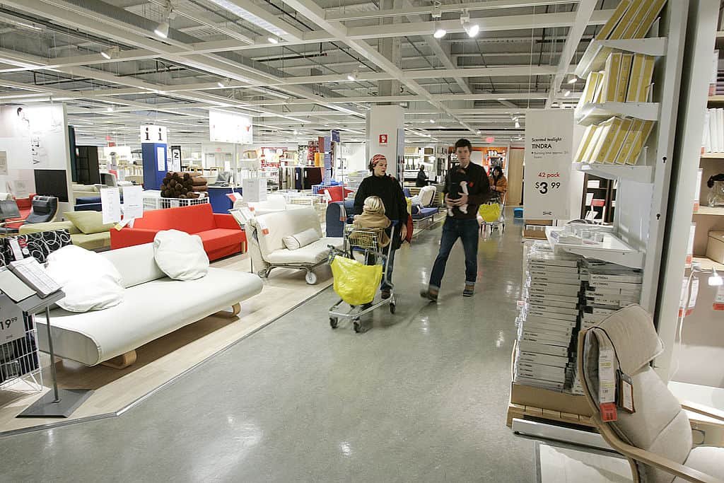 Twee mensen met een kar waarin een kind zit, lopen door het gangpad van een IKEA-winkel.