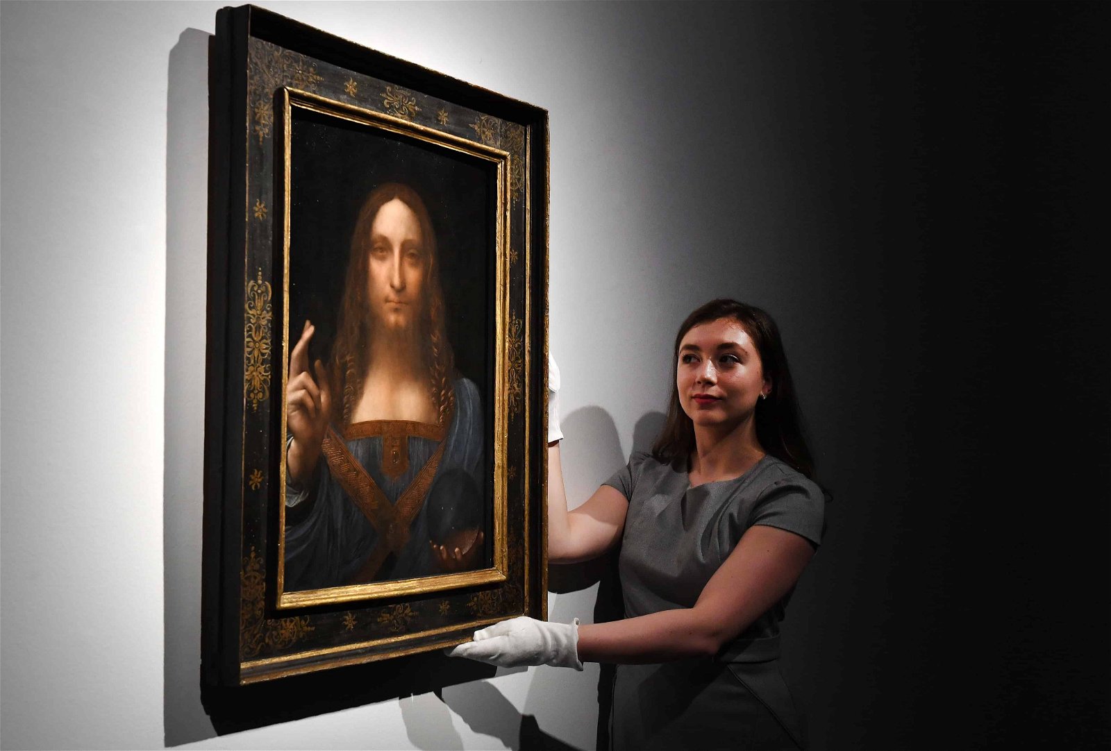 Een vrouw hangt het schilderij 'Salvator Mundi' van Leonardo da Vinci recht.