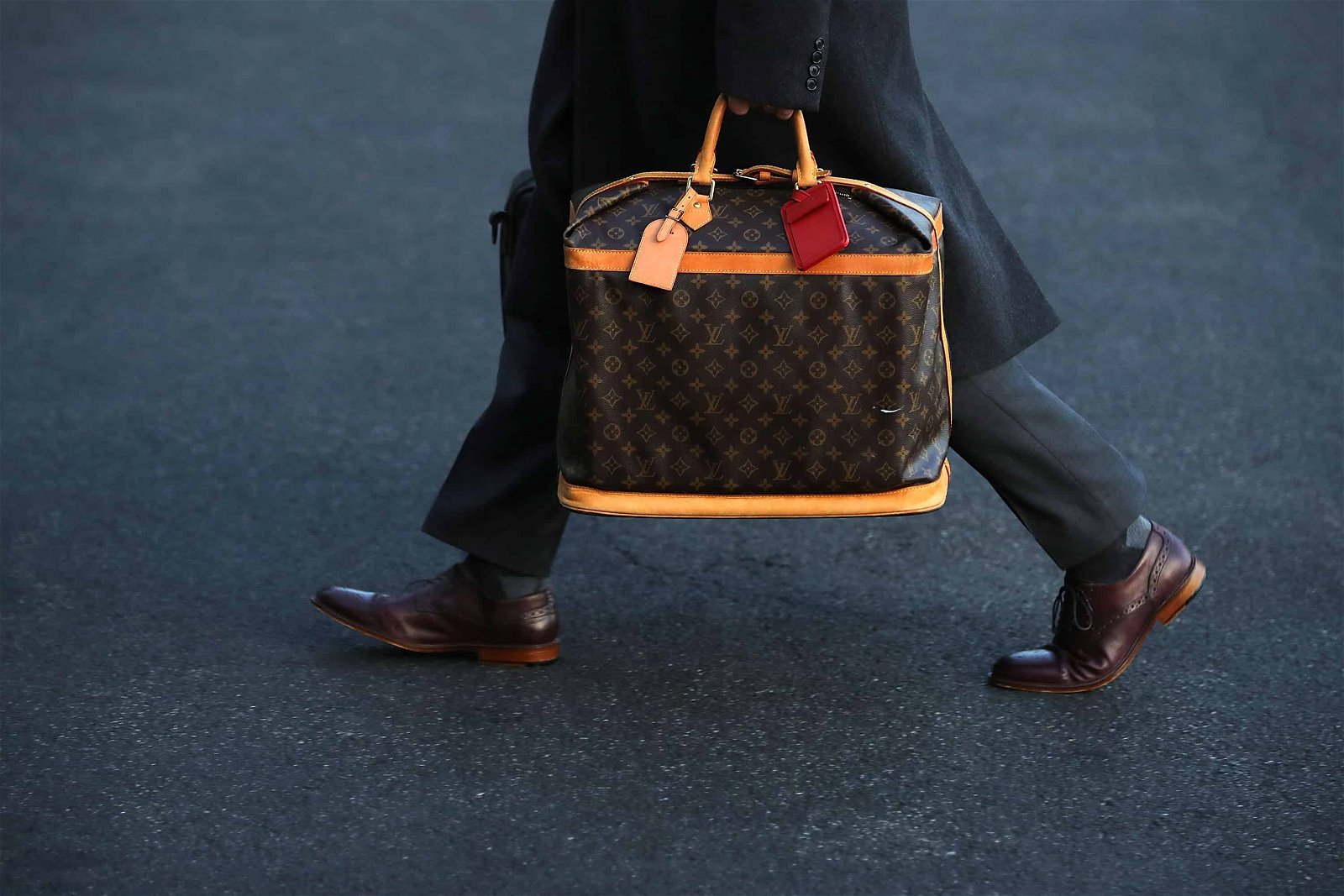 Een persoon loopt met een tas van Louis Vuitton over de straat.