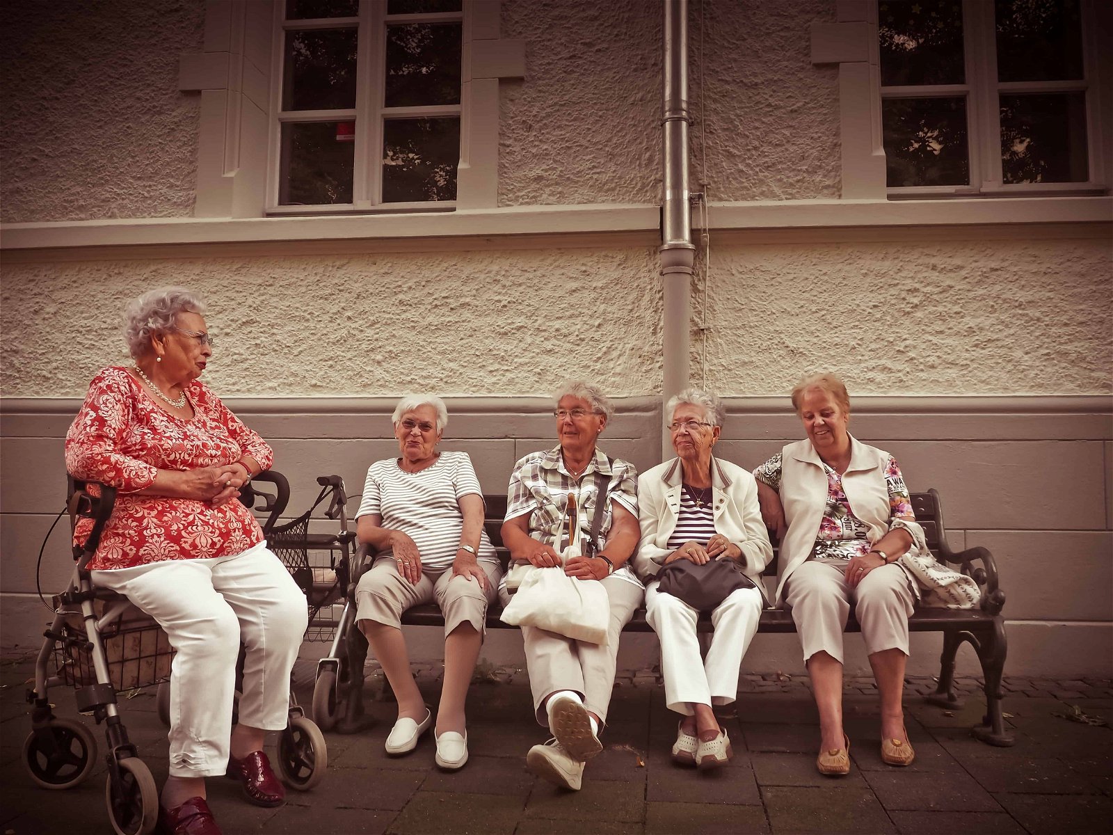 Une vieille femme en fauteuil roulant parle à quatre vieilles femmes assises sur un canapé.