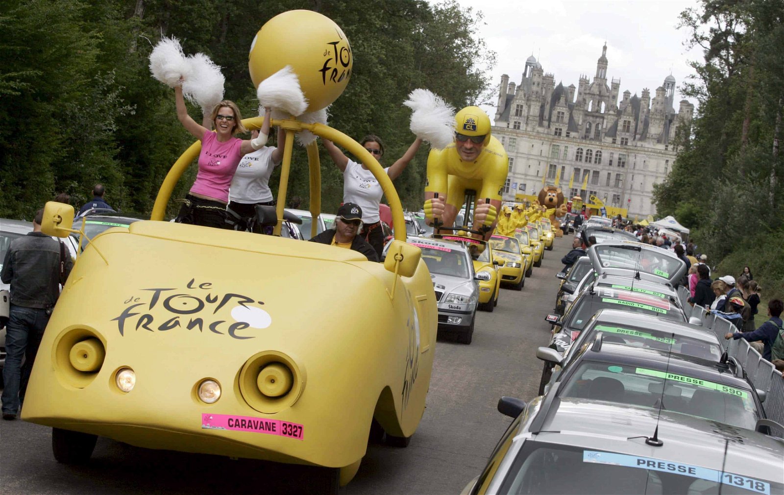 Een gele reclamewagen voert een lange karavaan tijdens de Tour de France aan.