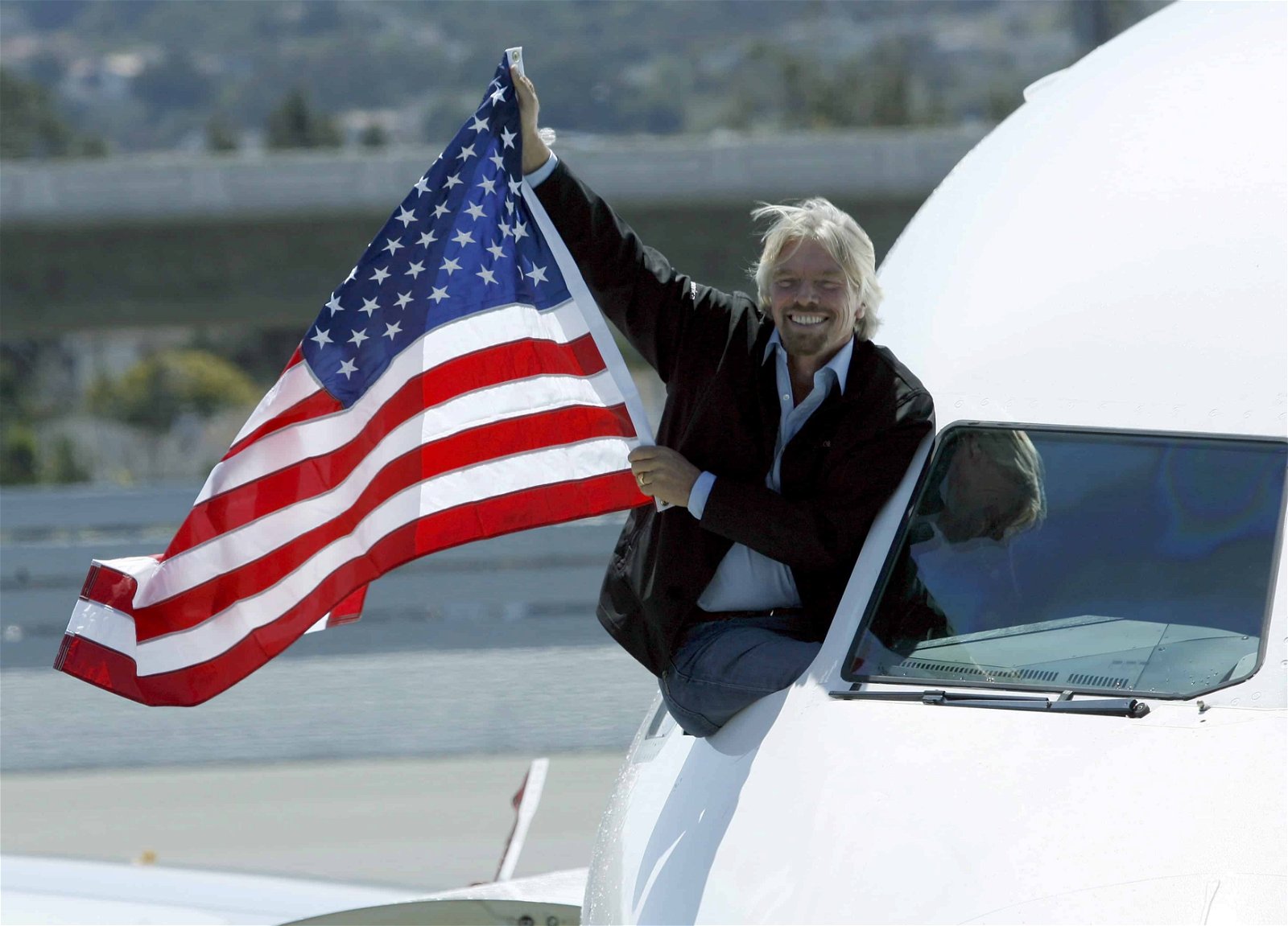Richard Branson houdt een Amerikaanse vlag vast vanuit een raam in de cockpit van een vliegtuig.