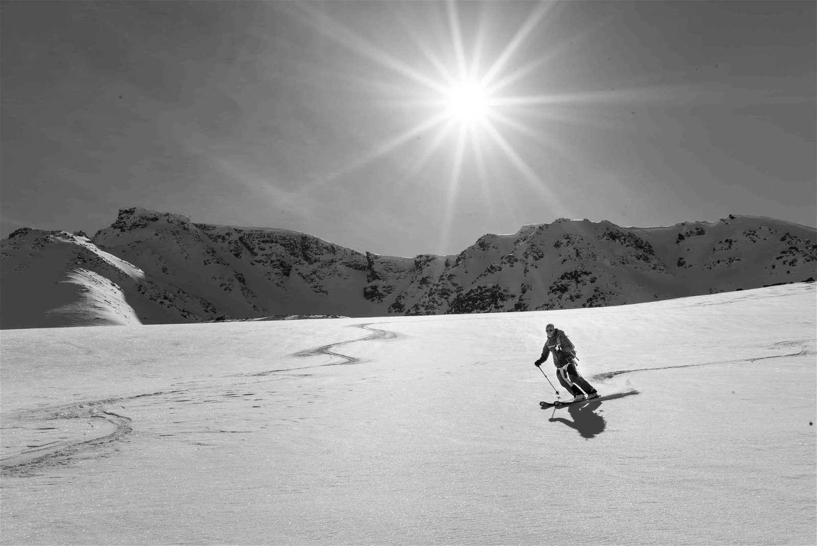 Een skiër op een zwart-wit foto glijdt over de sneeuw onder een stralende zon met bergtoppen op de achtergrond. Skiën is een van de favoriete hobby's van de superrijken.
