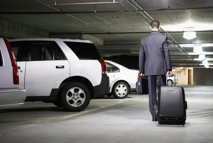 Young businessman with luggage in parking garage, rear view