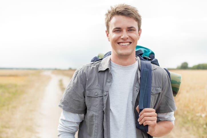 Portrait of happy male hiker with backpack standing on field