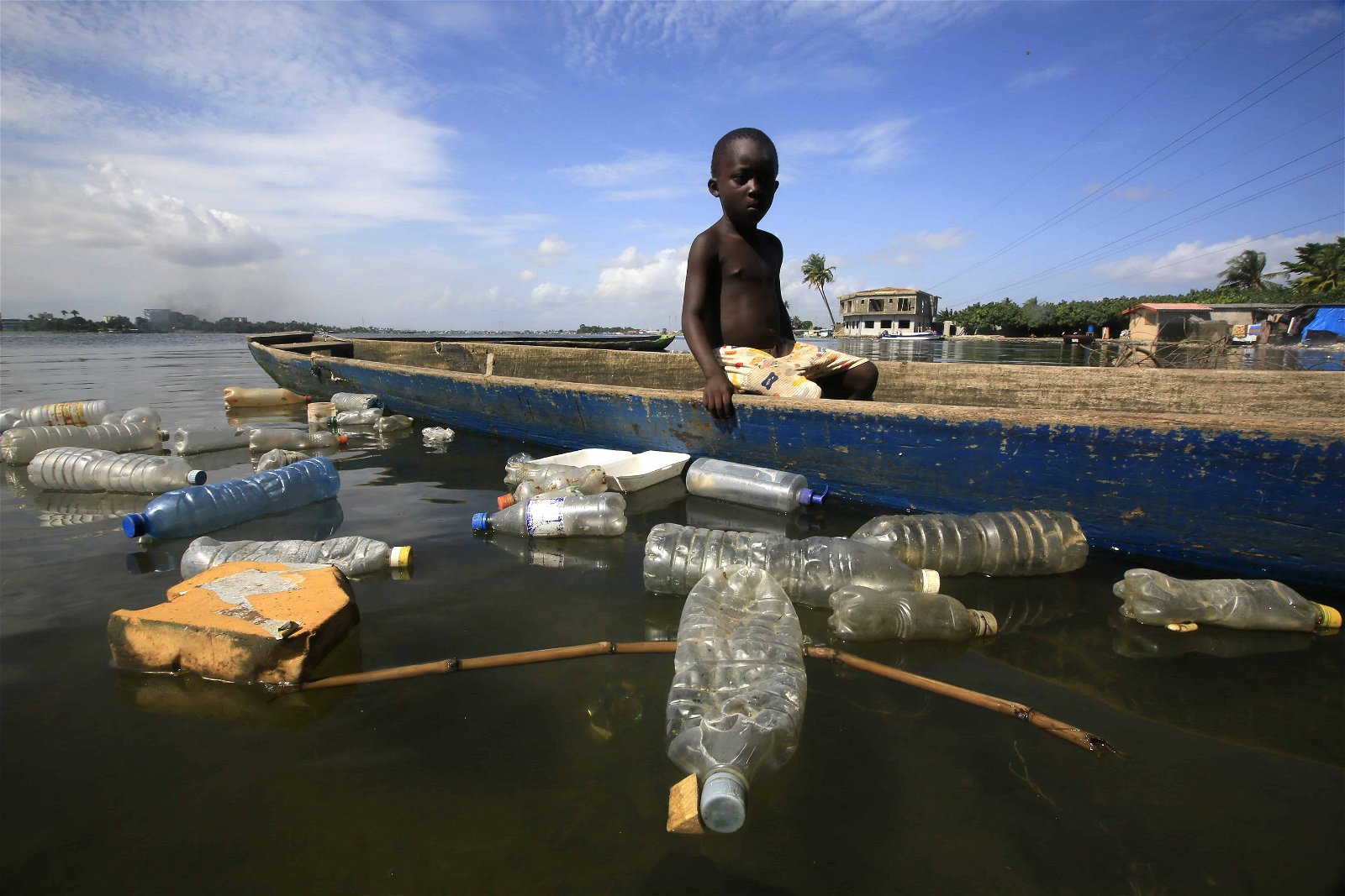 Een zwarte jongen wordt omringd door plastic in het water. Ook dit maakt deel uit van de globale watercrisis.