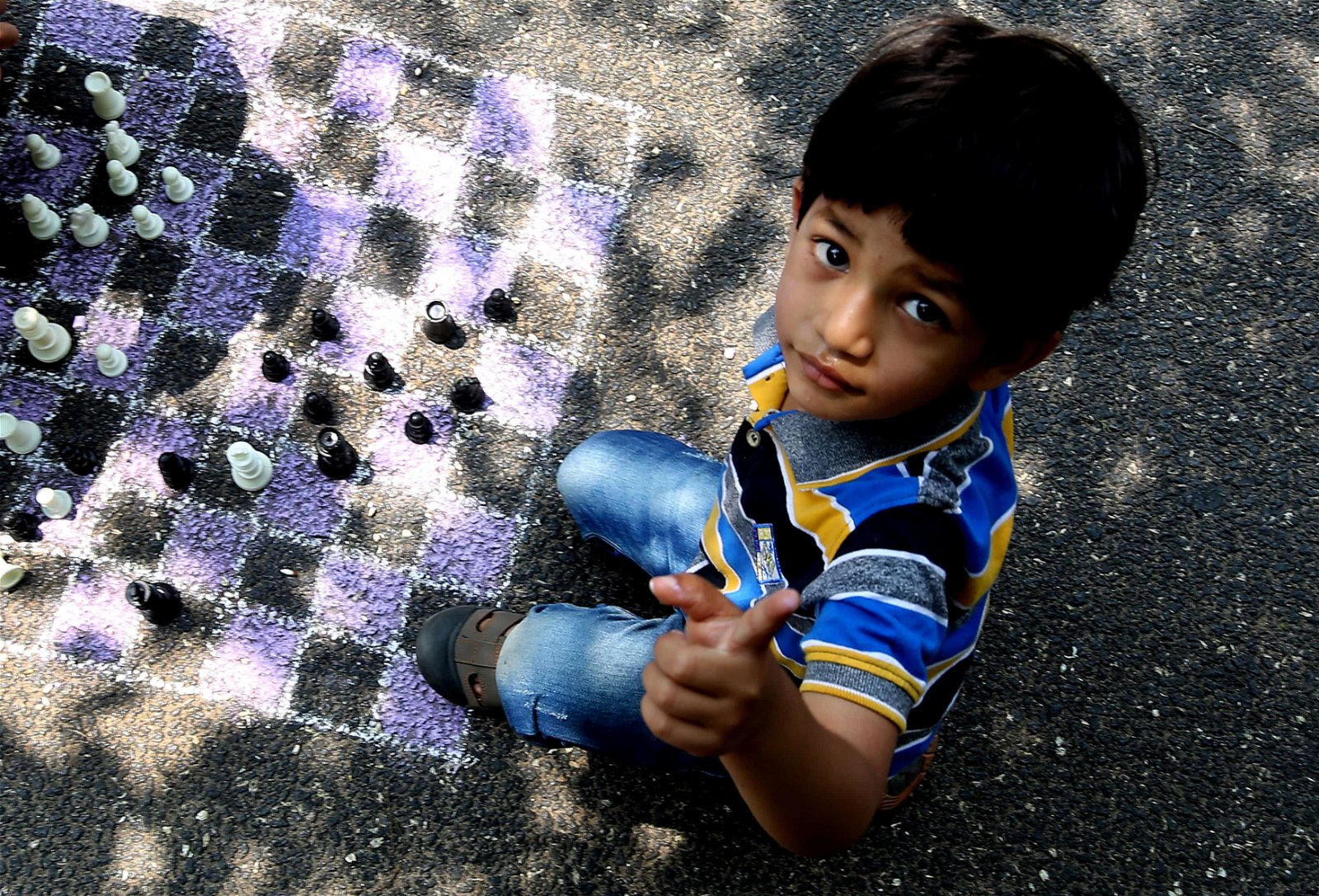 Een Indisch kinds wijst met z'n vinger omhoog tijdens een spelletje schaken. Het schaakbord is met krijt op het asfalt getekend.