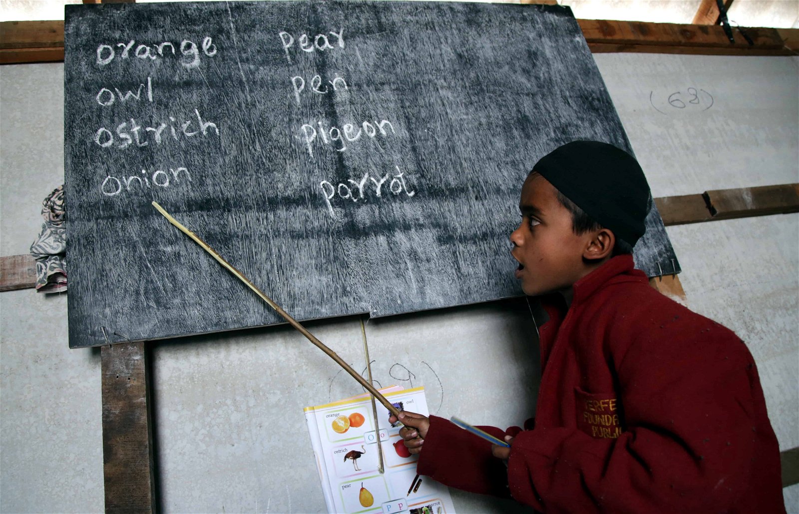 Een kind wijst met een stok naar een bord waar Engelstalige woorden op staan.