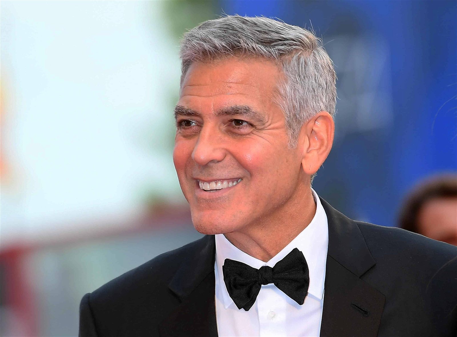 George Clooney in kostuum met strikje lacht.