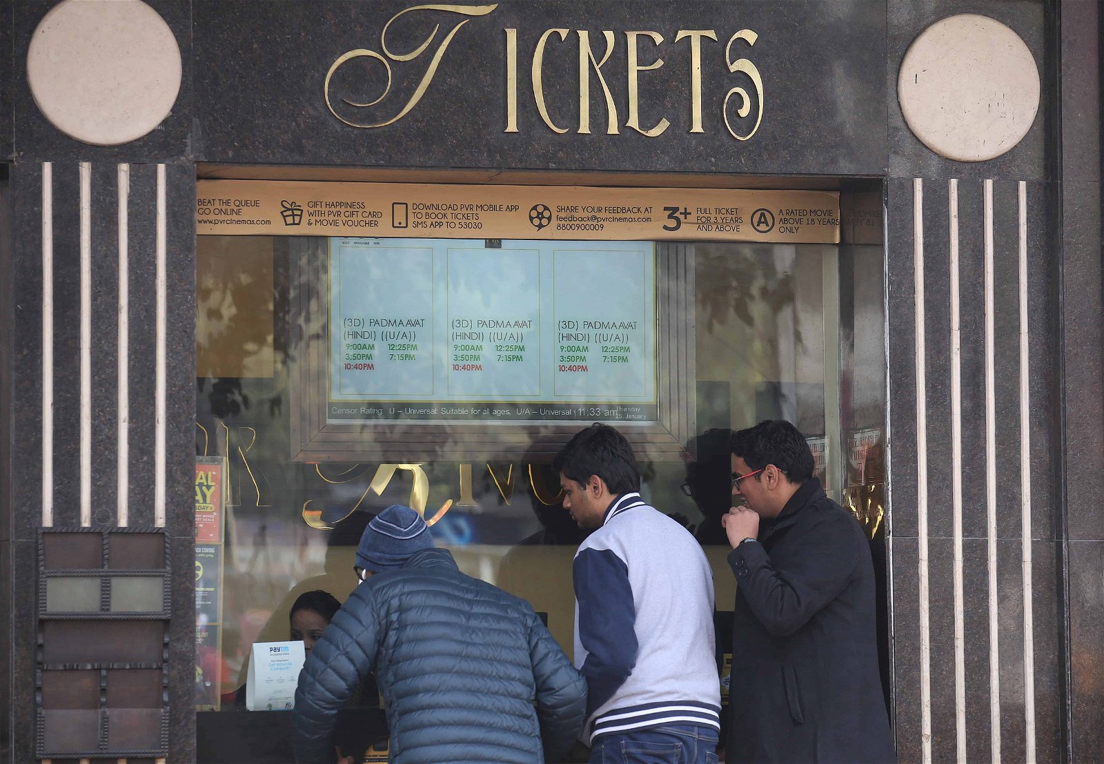 Drie mensen staan aan een kraampje voor bioscooptickets in India.