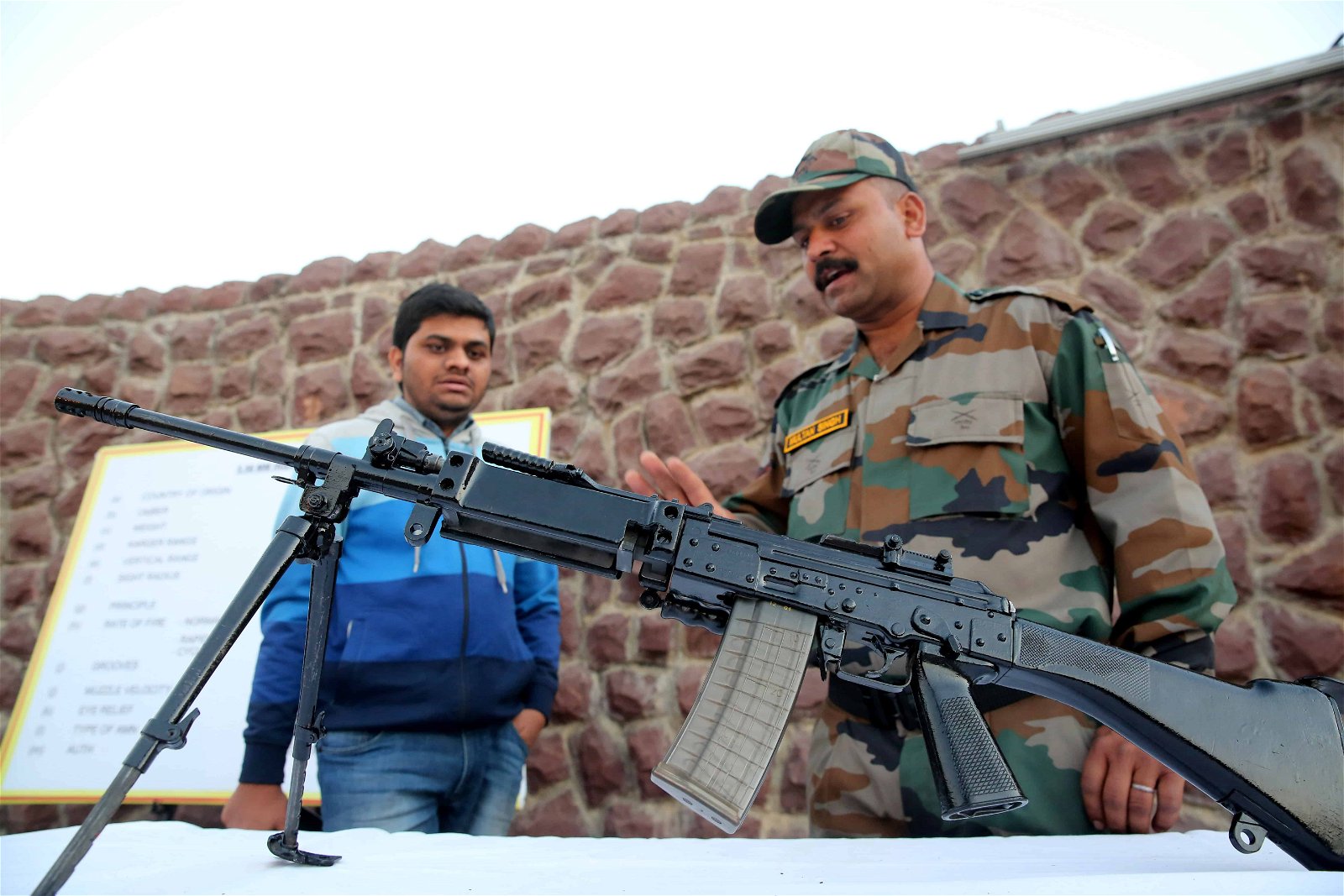 Een Indische soldaat legt een man uit hoe een machinegeweer werkt.