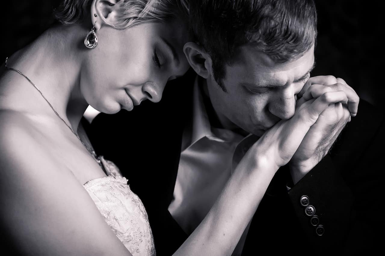 Een man kust de hand van een vrouw passioneel als teken van liefde op een zwartwit-beeld.