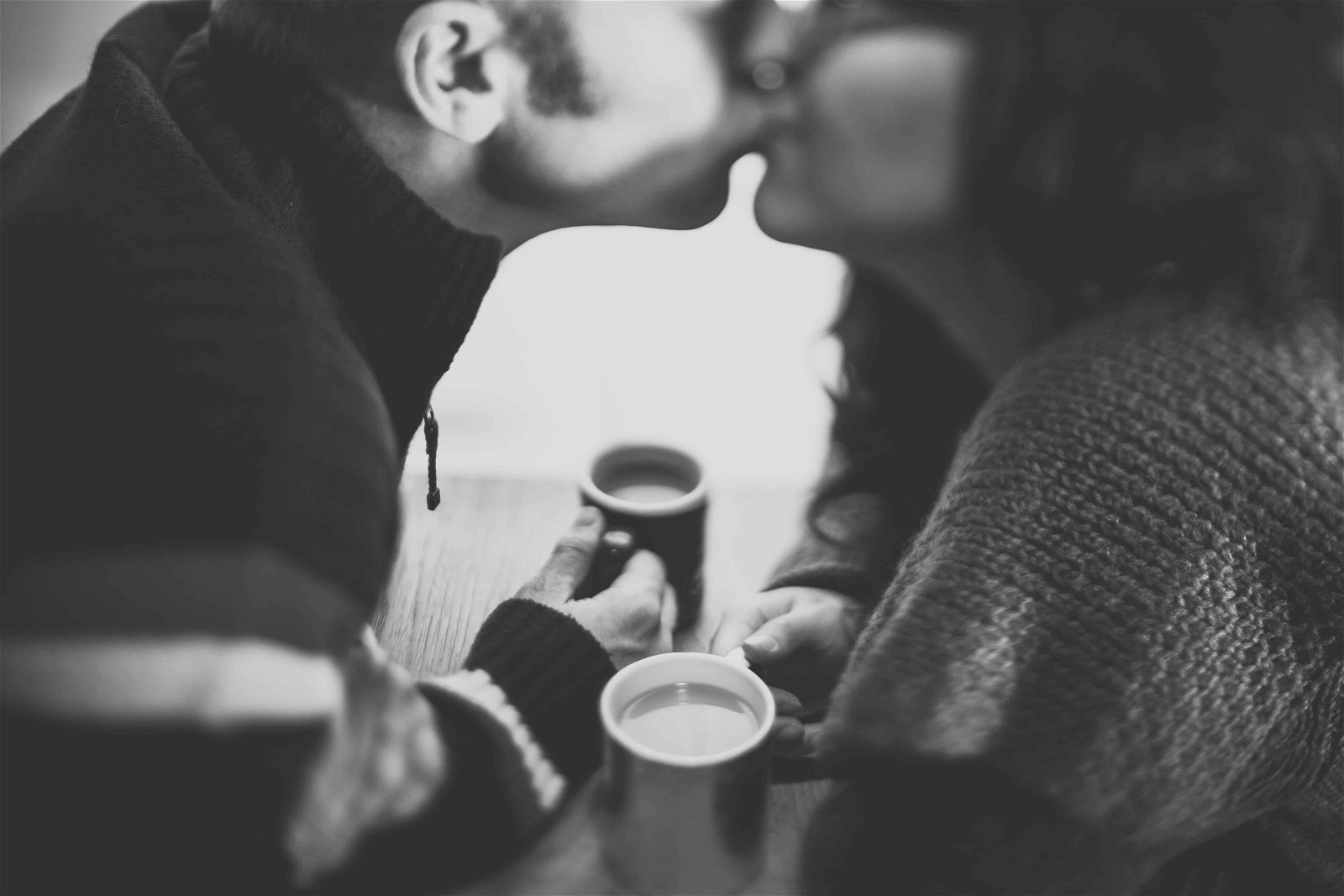 Zwart-wit foto van een man die zijn vrouw kust terwijl ze koffie drinken.