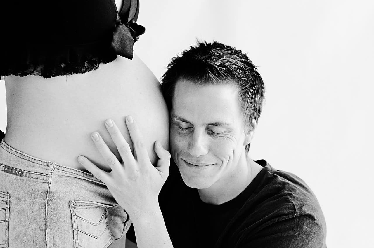 Een man houdt zijn hoofd tegen de buik van zijn zwangere vrouw. Ook bij mannen veranderen de hormonen.