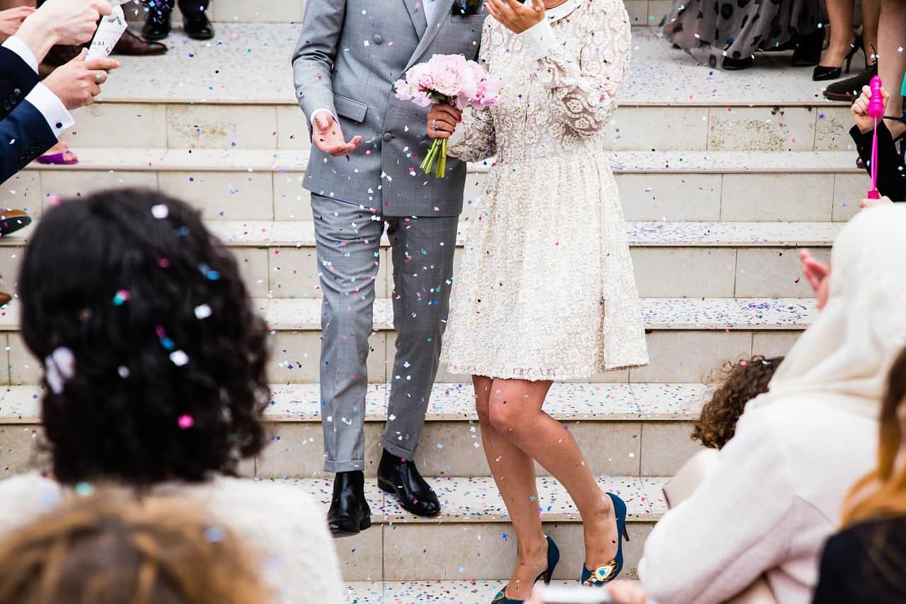 Een bruidegom en een bruid komen van de trappen naar beneden, terwijl confetti wordt geworpen.