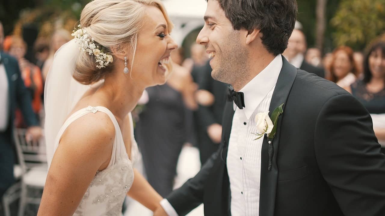 Een bruid en een bruidegom lachen naar elkaar.